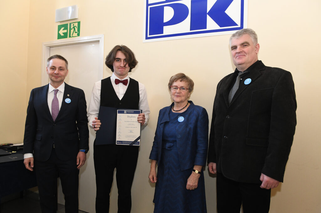Uczeń pozuje do wspólnego zdjęcia z pracownikami Politechniki Krakowskiej. W dłoniach trzyma dyplom