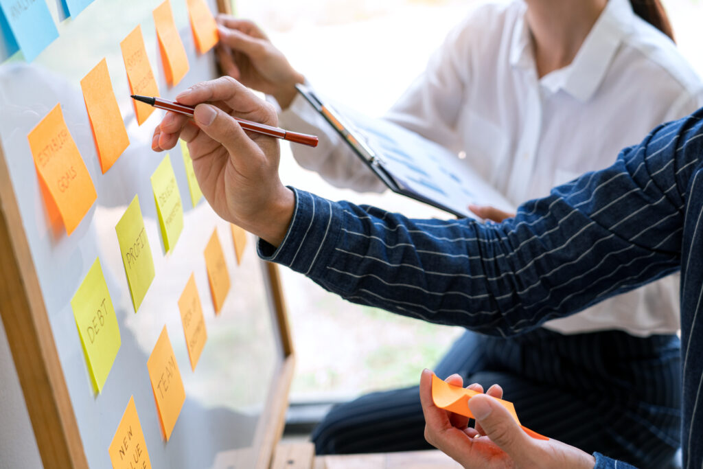 Dwoje ludzi aranżujący tablicę z notatkami na karteczkach samoprzylepnych