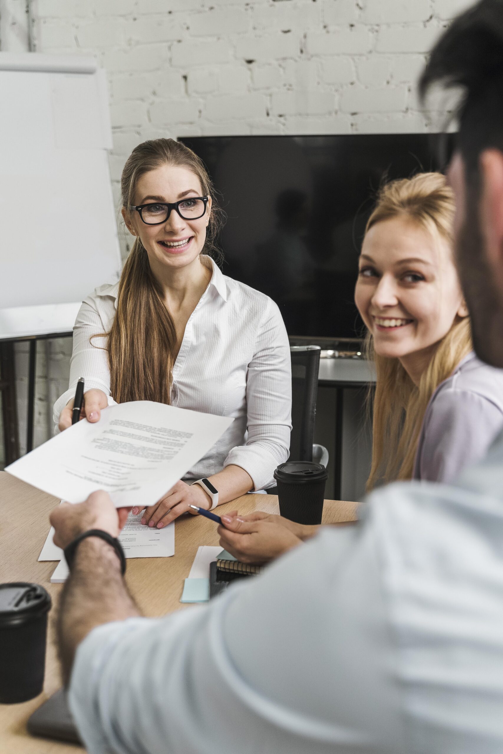 Dwie kobiety i mężczyzna uśmiechający się do siebie. Kobieta podaje mężczyźnie dokument.