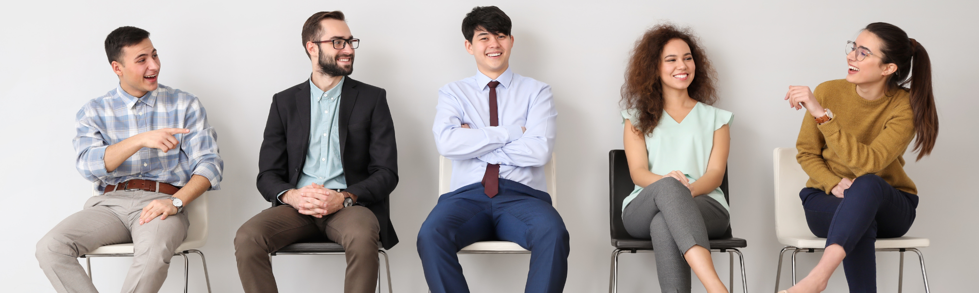 Grupa pięciu osób siedzi na stołkach i czeka. Trzech mężczyzn i dwie kobiety. Wszyscy się uśmiechają.