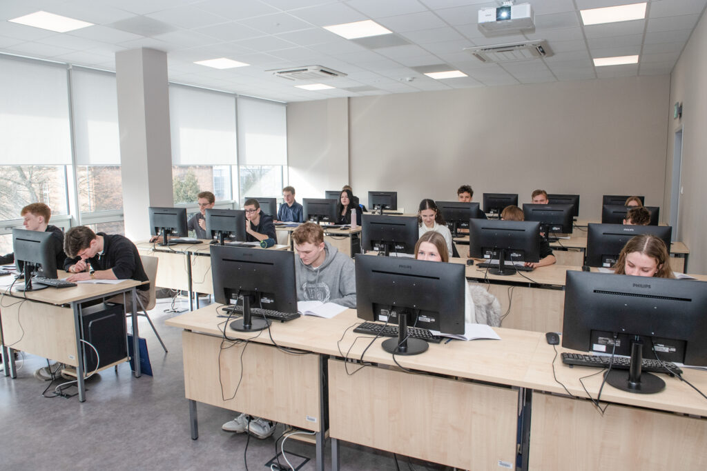 Jasna sala lekcyjna. Przy ławkach, na których stoją monitory, siedzą maturzyści i rozwiązują zadania.