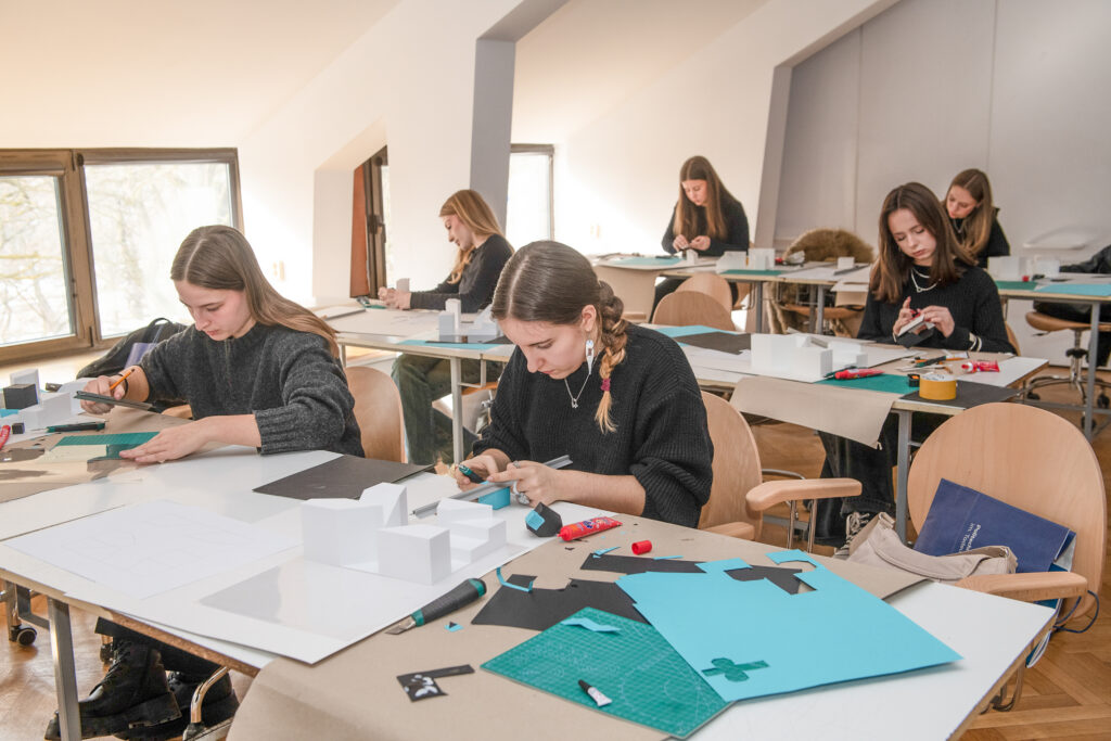 Sala lekcyjna. rząd stołów, przy których siedzą maturzyści i z kolorowych kartonów tworzą makiety.