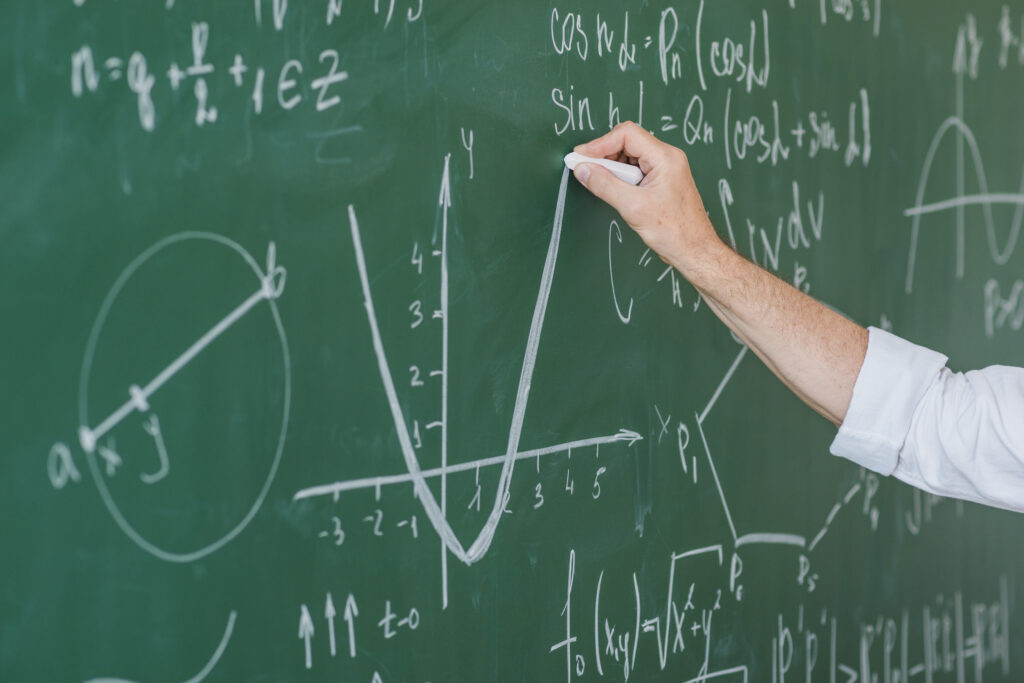 Męska ręka z kredą w dłoni, pisząca na tablicy równania matematyczne