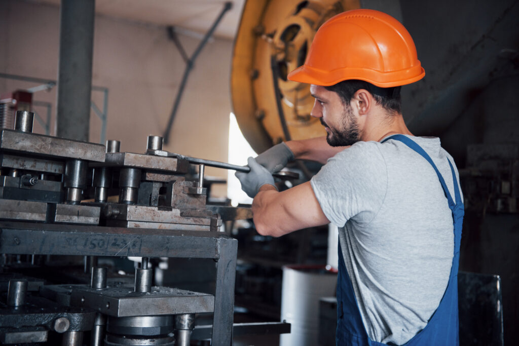 Mężczyzna w stroju roboczym i pomarańczowym kasku pracujący przy maszynie w fabryce